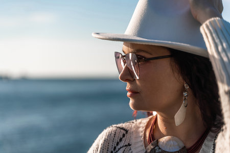 Portrait of a curly haired woman in a white hat and glasses on the background of the sea.