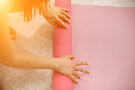 A young woman rolls a pink fitness or yoga mat before or after exercising, exercising at home in the living room or in a yoga studio. Healthy habits, keep fit, weight loss concept. Closeup photoの写真素材