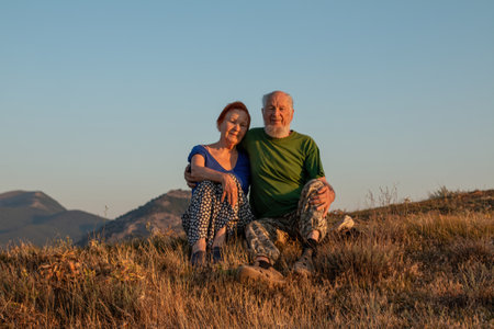 An elderly couple sits on a mountain with their backs with a beautiful view of the mountains in the distance.の写真素材