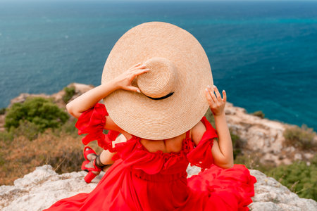 Woman in hat and red dress relaxes on the sea coast. Coastal area. During vacation. Capturing vacation moments scenic coastal setting, seaside view.の写真素材