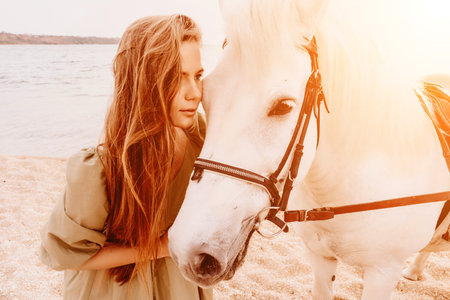 A woman in a dress stands next to a white horse on a beach, with the blue sky and sea in the background.の写真素材