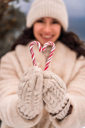 Woman candy sea. Smiling woman in knitted hat, mittens and beige coat holding lollipops candy canes...