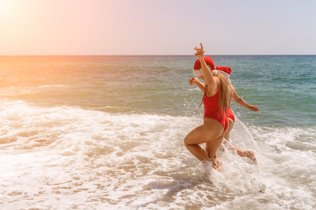 Women in Santa Claus hats run into the sea dressed in red swimsuits. Celebrating the New Year in a hot countryの写真素材