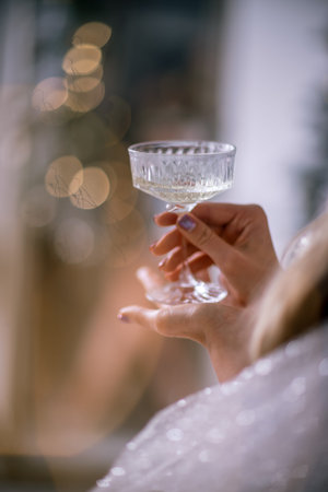 The hands of a woman hold a glass of champagne on a background of golden beke. The concept of the holiday, Christmas, new year, birthday.の写真素材