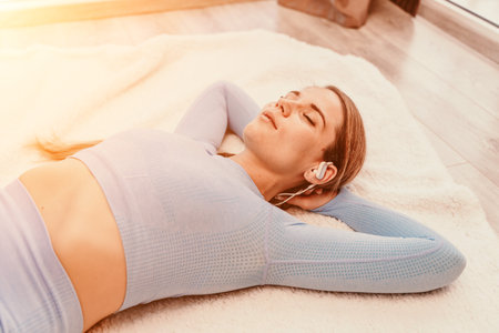 Top view portrait of relaxed woman listening to music with headphones lying on carpet at home. She is dressed in a blue tracksuit.の写真素材