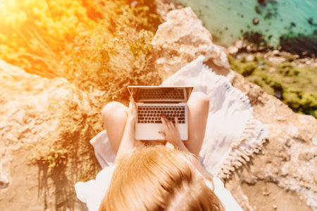 Freelance woman working on a laptop by the sea, typing away on the keyboard while enjoying the beautiful view, highlighting the idea of remote work.の写真素材