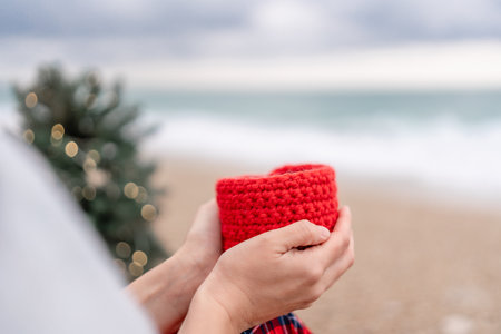 Sea Lady in plaid shirt with a red mug in her hands enjoys beach with Christmas tree. Coastal area. Christmas, New Year holidays concepの写真素材