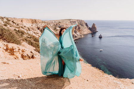 Woman green dress sea. Female dancer posing on a rocky outcrop high above the sea. Girl on the nature on blue sky background. Fashion photo.の写真素材