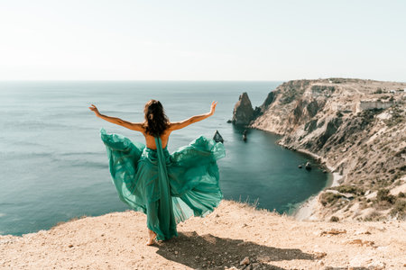 Woman green dress sea. Female dancer posing on a rocky outcrop high above the sea. Girl on the nature on blue sky background. Fashion photo.の写真素材