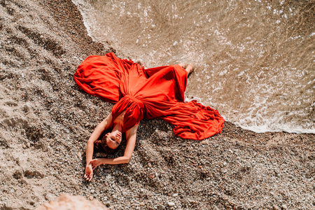 Woman red dress sea. Female dancer in a long red dress posing on a beach with rocks on sunny dayの写真素材