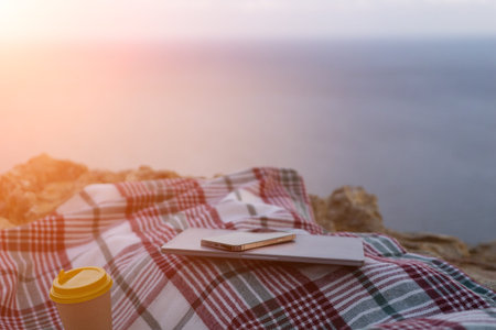 Laptop coffee on blanket with ocean view. Illustrating serene outdoor laptop use. Freelancer...