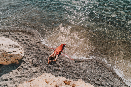 Woman red dress sea. Female dancer in a long red dress posing on a beach with rocks on sunny dayの写真素材