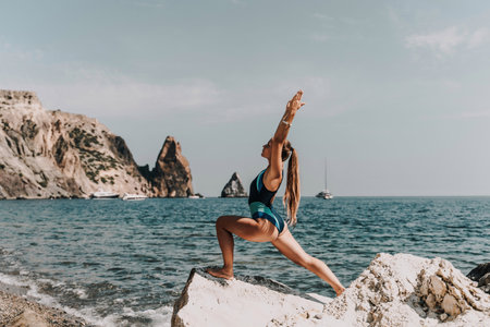 Yoga on the beach. A happy woman meditating in a yoga pose on the beach, surrounded by the ocean and rock mountains, promoting a healthy lifestyle outdoors in nature, and inspiring fitness concept.の写真素材