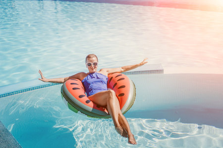 Happy woman in a swimsuit and sunglasses floating on an inflatable ring in the form of a watermelon,...
