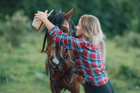 Happy blonde with horse in forest. Woman and a horse walking through the field during the day. Dressed in a plaid shirt and black leggings.の写真素材