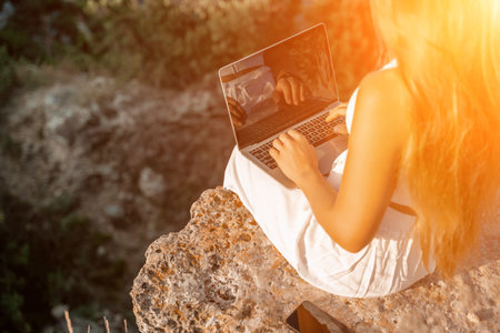 Freelance happy woman typing on her laptop, enjoying the picturesque sea view, highlighting the idea of working remotely with a relaxed and pleasant atmosphere.の写真素材