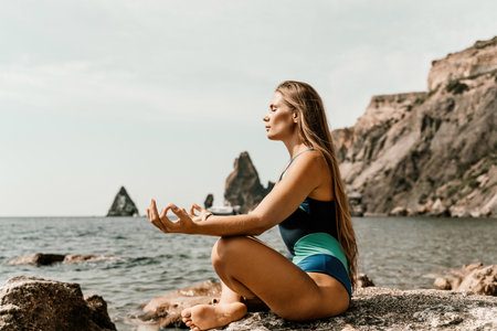 Yoga on the beach. A happy woman meditating in a yoga pose on the beach, surrounded by the ocean and rock mountains, promoting a healthy lifestyle outdoors in nature, and inspiring fitness concept.の写真素材