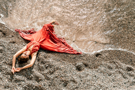 Woman red dress sea. Female dancer in a long red dress posing on a beach with rocks on sunny dayの写真素材