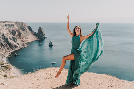 Woman green dress sea. Female dancer posing on a rocky outcrop high above the sea. Girl on the nature on blue sky background. Fashion photo.の写真素材