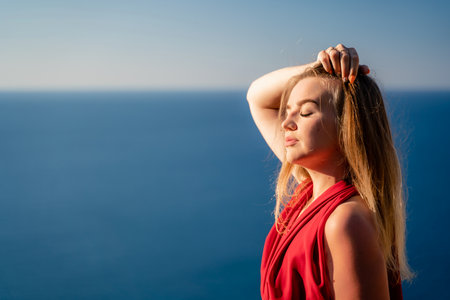 A woman in a red flying dress fluttering in the wind, against the backdrop of the sea.の写真素材