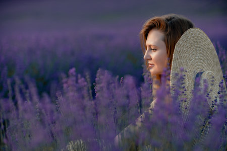 Woman poses in lavender field at sunset. Happy woman in yellow dress holds lavender bouquet. Aromatherapy concept, lavender oil, photo session in lavenderの写真素材