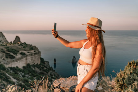Selfie woman in hat, white tank top and shorts makes selfie shot mobile phone post photo social network outdoors on sea background beach people vacation lifestyle travel concept.の写真素材