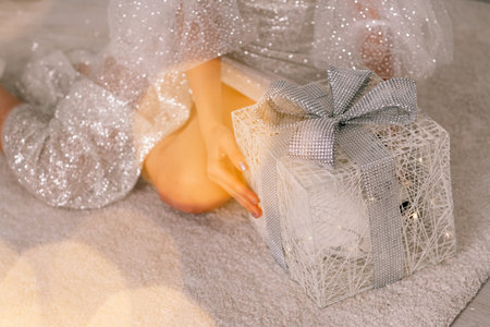 A beautiful box with a gift in the hands of a girl, she sits in a brilliant dress and holds it in her hands. Bokeh from garlands.の写真素材