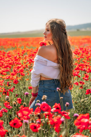 Woman poppies field. Side view of a happy woman with long hair in a poppy field and enjoying the beauty of nature in a warm summer day.の写真素材