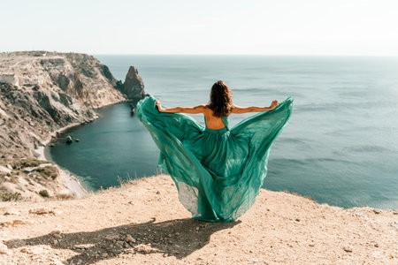 Woman green dress sea. Female dancer posing on a rocky outcrop high above the sea. Girl on the nature on blue sky background. Fashion photo.の写真素材