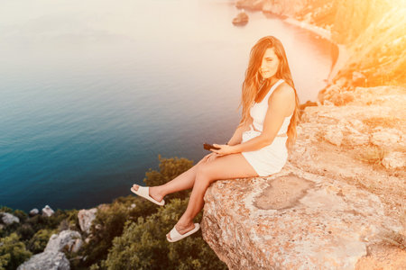 Happy woman in white shorts and T-shirt, with long hair, talking on the phone while enjoying the scenic view of the sea in the background.の写真素材