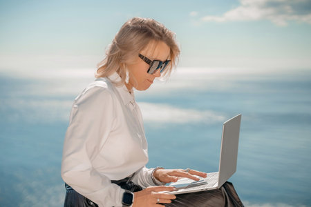Business woman on nature in white shirt and black skirt. She works with an iPad in the open air with a beautiful view of the sea. The concept of remote work.の写真素材