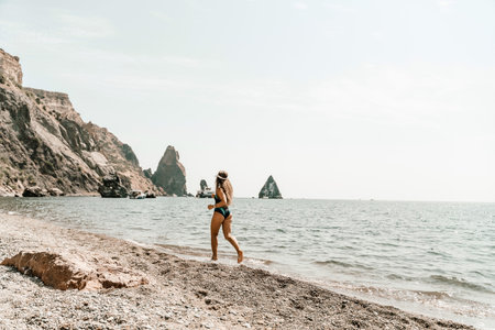 Woman beach vacation photo. A happy tourist in a blue bikini enjoying the scenic view of the sea and volcanic mountains while taking pictures to capture the memories of her travel adventure.の写真素材