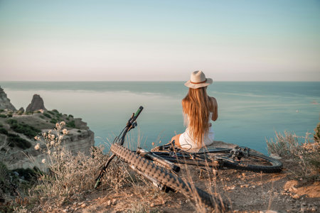 A woman cyclist on a mountain bike looking at the landscape of mountains and sea. Adventure travel on bike.の写真素材
