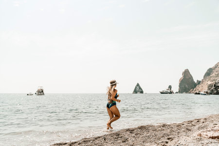 Woman beach vacation photo. A happy tourist in a blue bikini enjoying the scenic view of the sea and volcanic mountains while taking pictures to capture the memories of her travel adventure.の写真素材