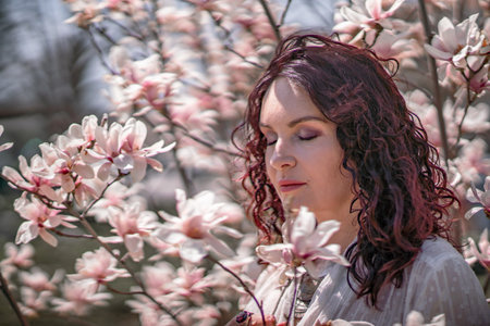 Magnolia park woman. Stylish woman in a hat stands near the magnolia bush in the park. Dressed in white corset pants and posing for the camera.の写真素材