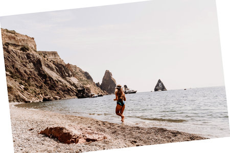 Woman beach vacation photo. A happy tourist in a blue bikini enjoying the scenic view of the sea and volcanic mountains while taking pictures to capture the memories of her travel adventure.の写真素材