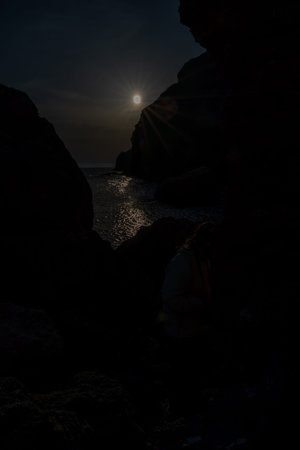 Woman tourist enjoying the sunset over the sea mountain landscape. Sits outdoors on a rock above the...