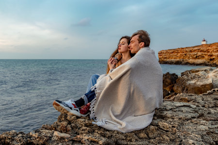 Portraits of lovers, romantic couple of lovers hugging, kissing, touching, eye contact at sunset, sunrise against the background of the sea, sun, clouds in fiery red, orange colorsの写真素材