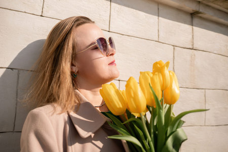 Woman holding yellow tulips, leaning against stone wall. Womens holiday concept, giving flowers.