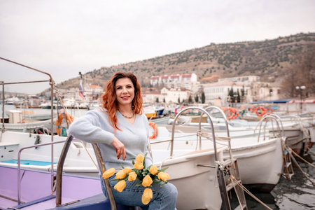 Woman holds yellow tulips in harbor with boats docked in the background., overcast day, yellow sweater, mountainsの写真素材