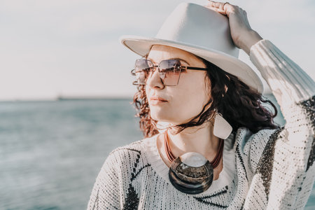 Portrait of a curly haired woman in a white hat and glasses on the background of the sea.