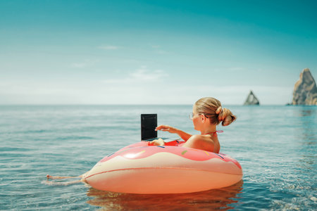 Woman laptop sea. Freelancer woman in sunglases floating on an inflatable big pink donut with a laptop in the sea. People summer vacation rest lifestyle conceptの写真素材