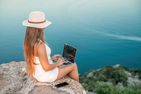 Freelance women sea working on the computer. Good looking middle aged woman typing on a laptop keyboard outdoors with a beautiful sea view. The concept of remote work.の写真素材
