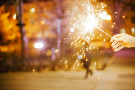 Woman holding sparkler night while celebrating Christmas outside. Dressed in a fur coat and a red headband. Blurred christmas decorations in the background. Selective focusの写真素材