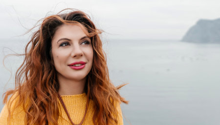 Portrait windswept hair happy woman against a backdrop of mountains and sea. Daylight illuminates...