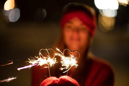 Woman holding sparkler night while celebrating Christmas outside. Dressed in a fur coat and a red...