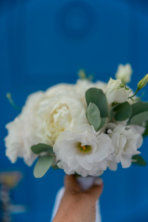 A bouquet of white flowers is being held by a person. The flowers are arranged in a vase and are placed on a blue background. The bouquet has a simple and elegant design.の写真素材