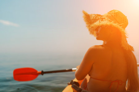 A woman wearing a straw hat is paddling a canoe on a sunny day. Scene is relaxed and carefree, as the woman enjoys her time on the water.の写真素材