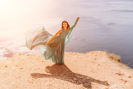 Woman green dress sea. Female dancer posing on a rocky outcrop high above the sea. Girl on the...
