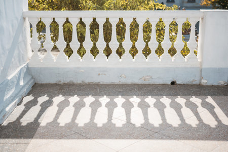 A balcony with a railing and a tree in the background. The railing is white and has a shadow on it.